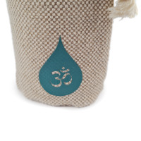 Bližnji pogled na tkanino vrečke iz bombaža in konoplje ter vezen logotip Om na steklenici OmWater.