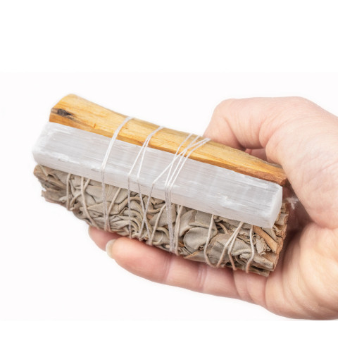 Ročno zvit beli žajbelj, palčka palo santo in kristal selenit, povezani z belo vrvico, v dlani na belem ozadju.